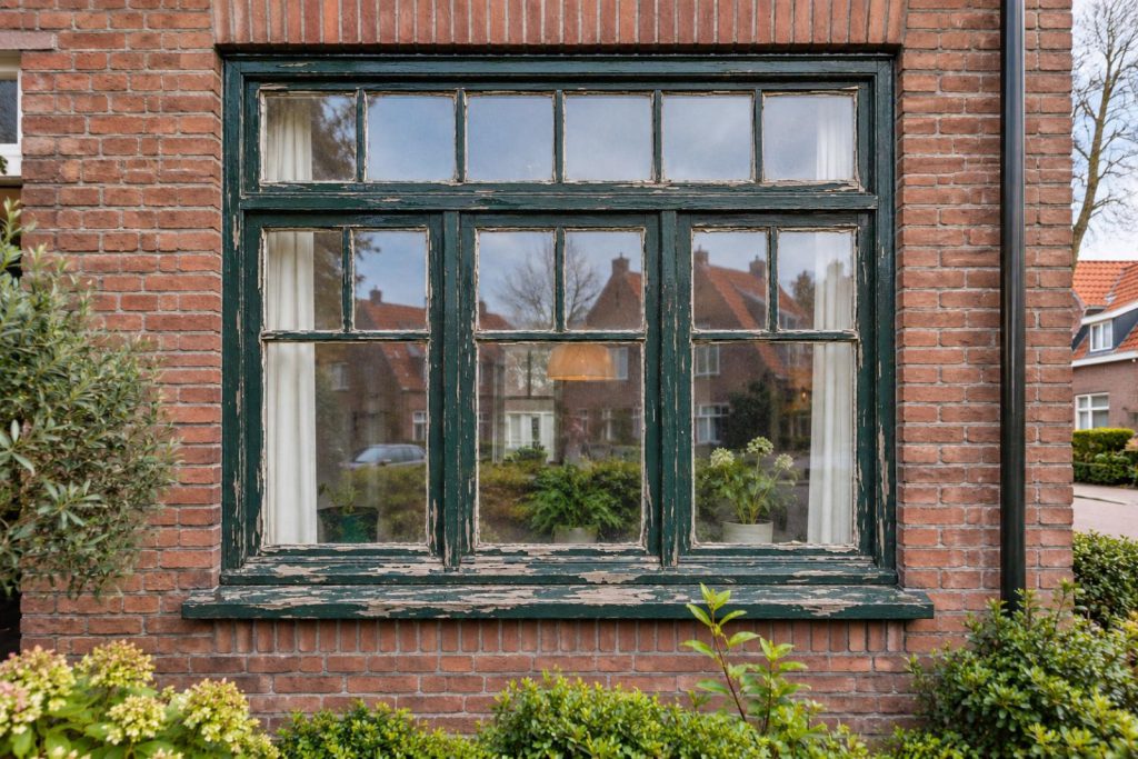 Kozijn met afgebladderde groene verf, voor het schilderwerk